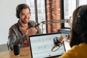 Two podcasters in headphones laughin while recording audio podcast